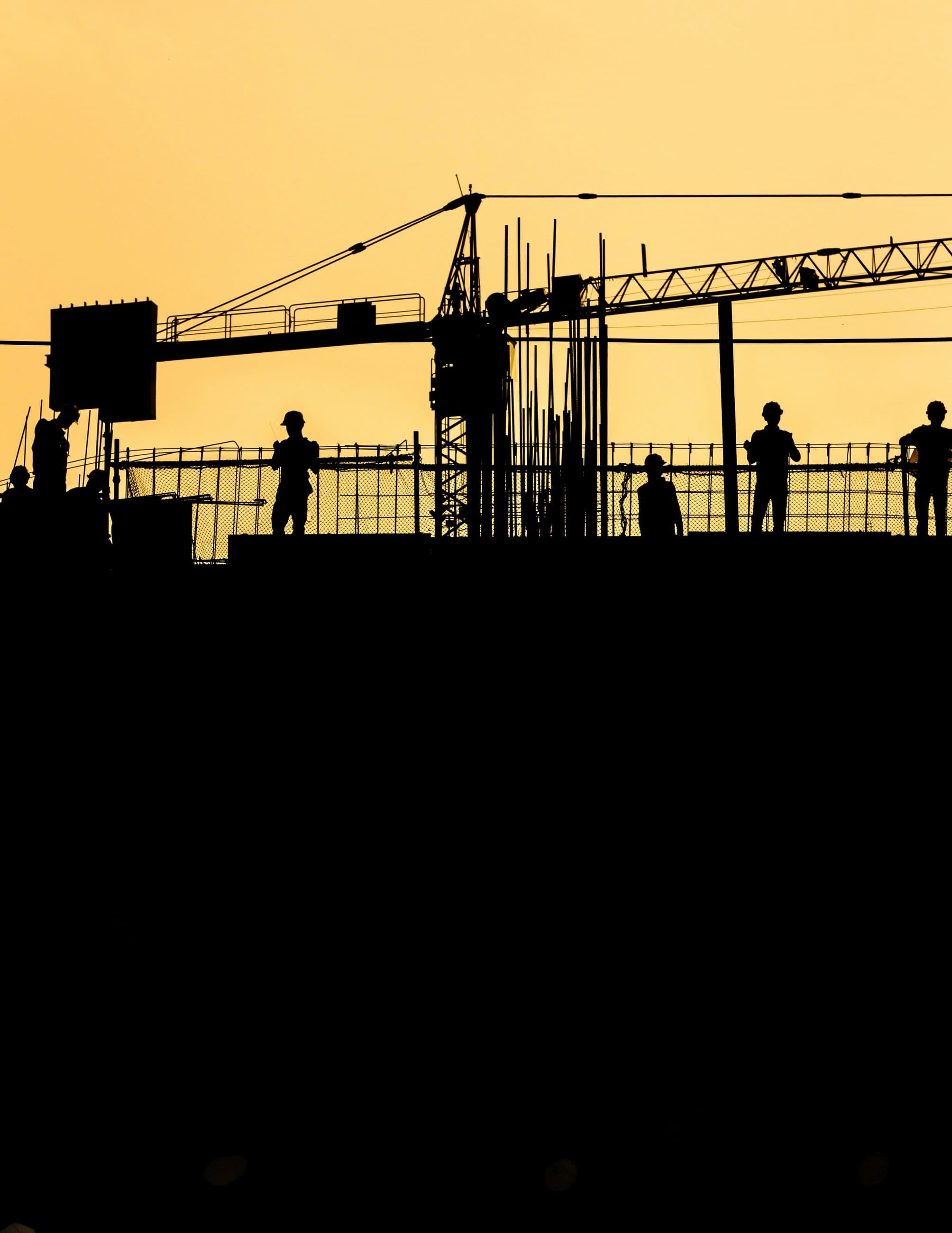 Crew and crane silhouetted against a sunset over a construction deck